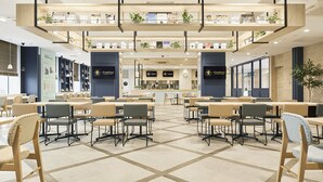 A spacious indoor area with multiple tables and chairs, a central counter, and a mezzanine level with plants and signage. - Keikyu EX INN Haneda Innovation City (Tokyo)