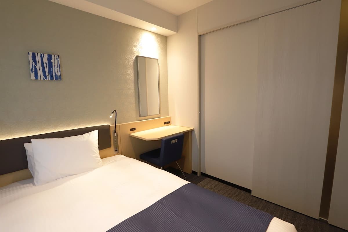 Een hotelkamer met een bed, nachtkastje, spiegel en een schuifdeur.