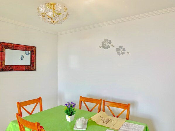 A dining area with a green table, wooden chairs, a chandelier, a framed artwork, and wall decals.