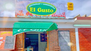 Ein Restaurant namens El Gusto mit einer grünen Markise, einer sichtbaren Speisekarte an der Wand und einer Ziegel-Fassade.