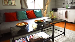 A modern living room with a sofa, cushions, a glass coffee table, and a kitchen area in the background. - Nagomiya Kyoto Gion (Kyoto)