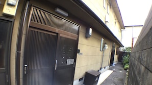 A narrow alleyway with a building featuring a large metal gate and a small black trash bin. - Nagomiya Kyoto Gion (Kyoto)