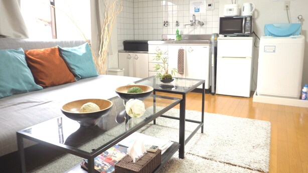 A modern kitchen with white cabinets, a microwave, and a refrigerator. There is a glass table with bowls and a plant. - Nagomiya Kyoto Gion (Kyoto)