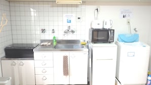 A kitchen with white cabinets, a microwave, a sink, and a refrigerator. There are signs on the wall and a bottle of dish soap on the counter. - Nagomiya Kyoto Gion (Kyoto)