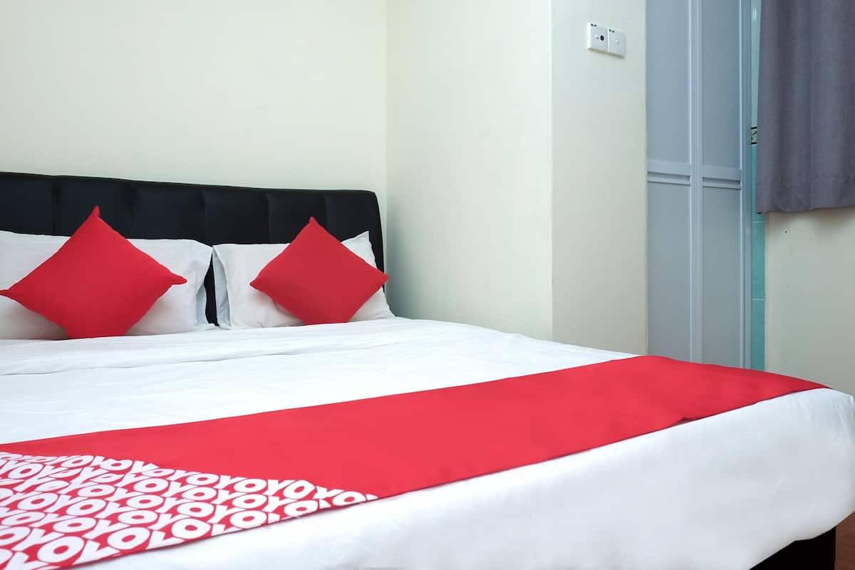 Een opgemaakt bed met een wit-rode spreideken, twee rode kussens en een zwart hoofdeinde.
