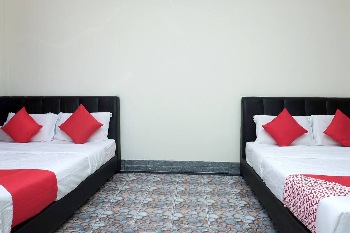 Een hotelkamer met twee bedden, elk voorzien van witte lakens en rode kussens, en een betegelde vloer.