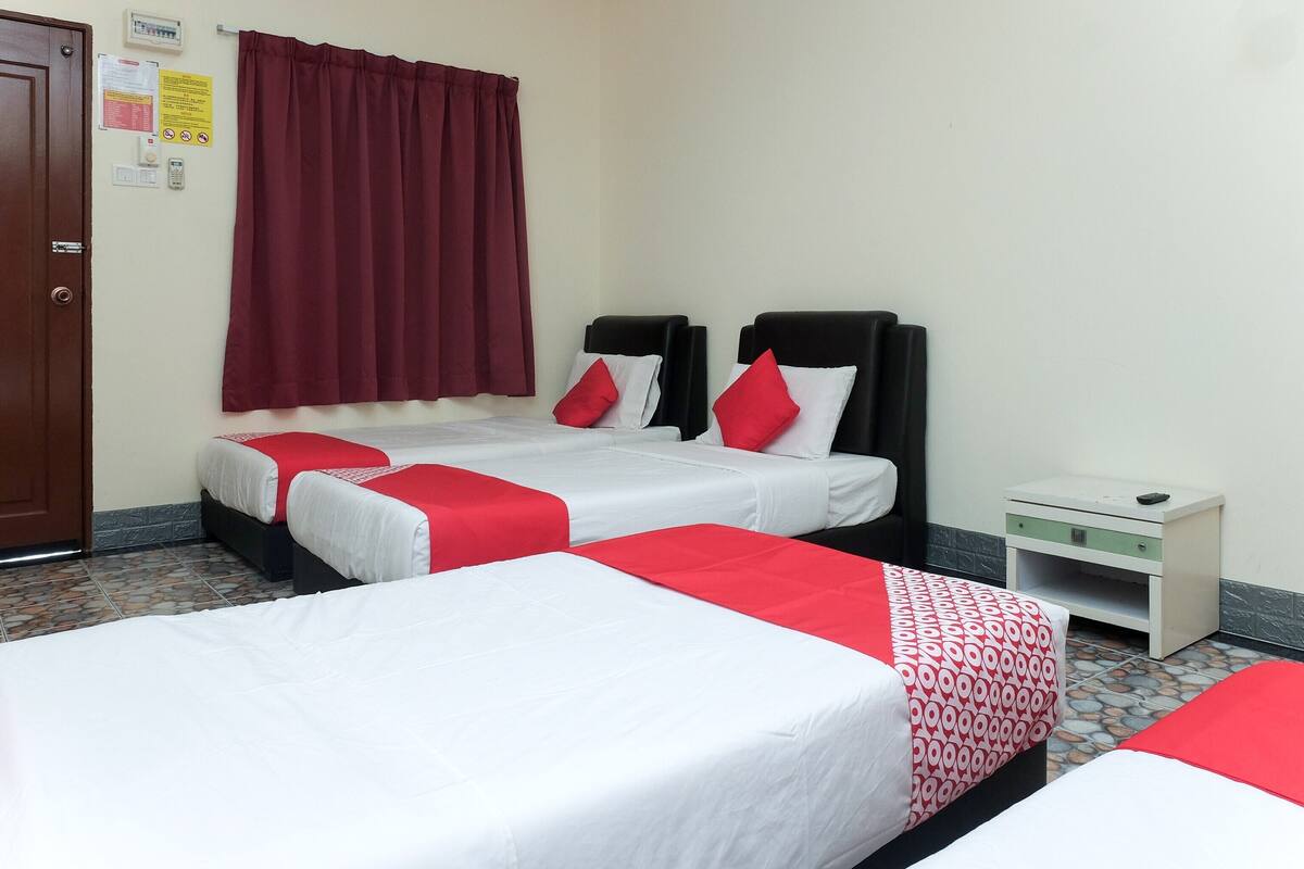 Een hotelkamer met twee bedden, elk voorzien van rood-witte beddengoed, een klein nachtkastje en een rood gordijn.