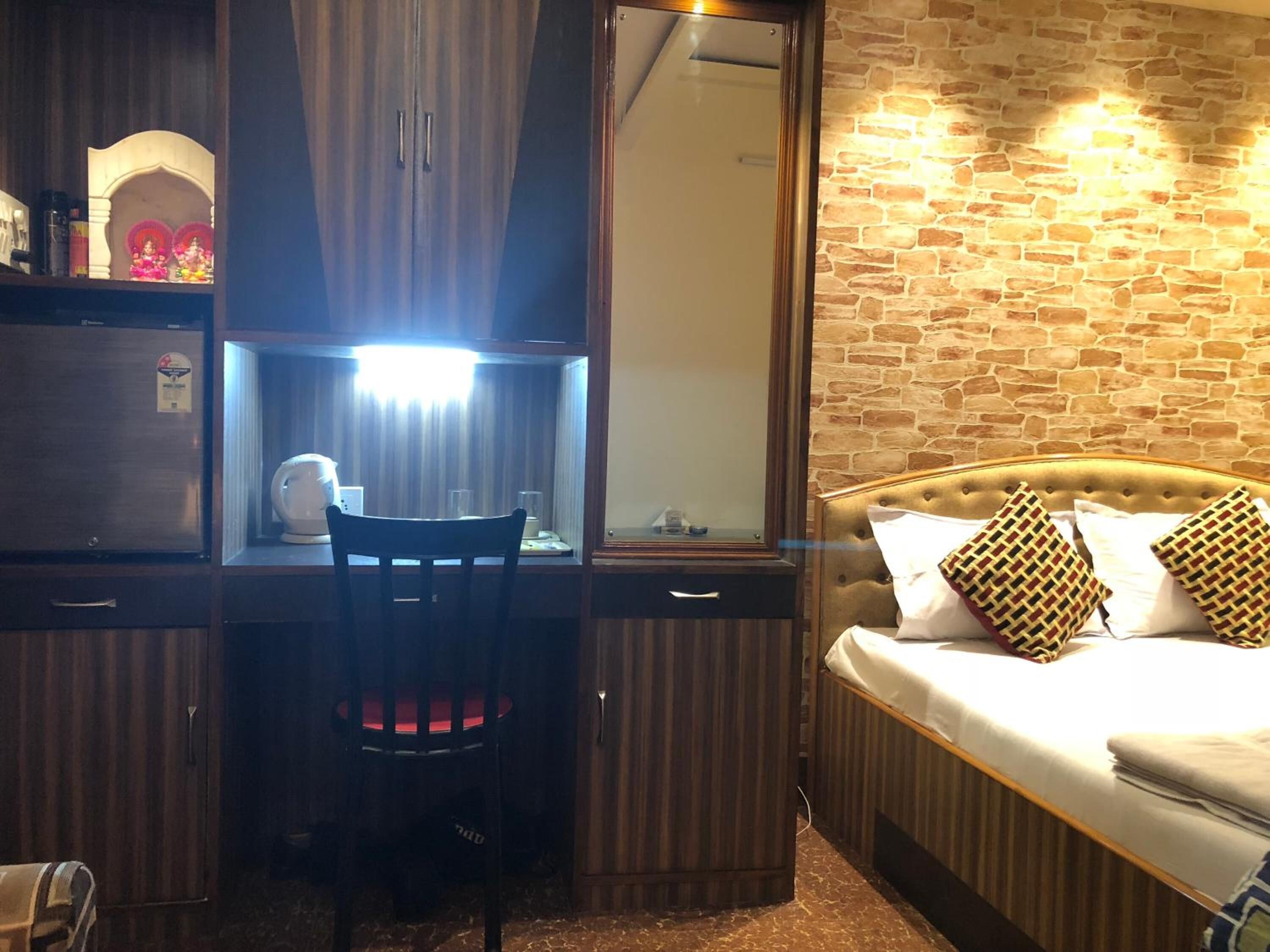 A hotel room with a bed, a desk with a chair, a wardrobe, and a mirror.