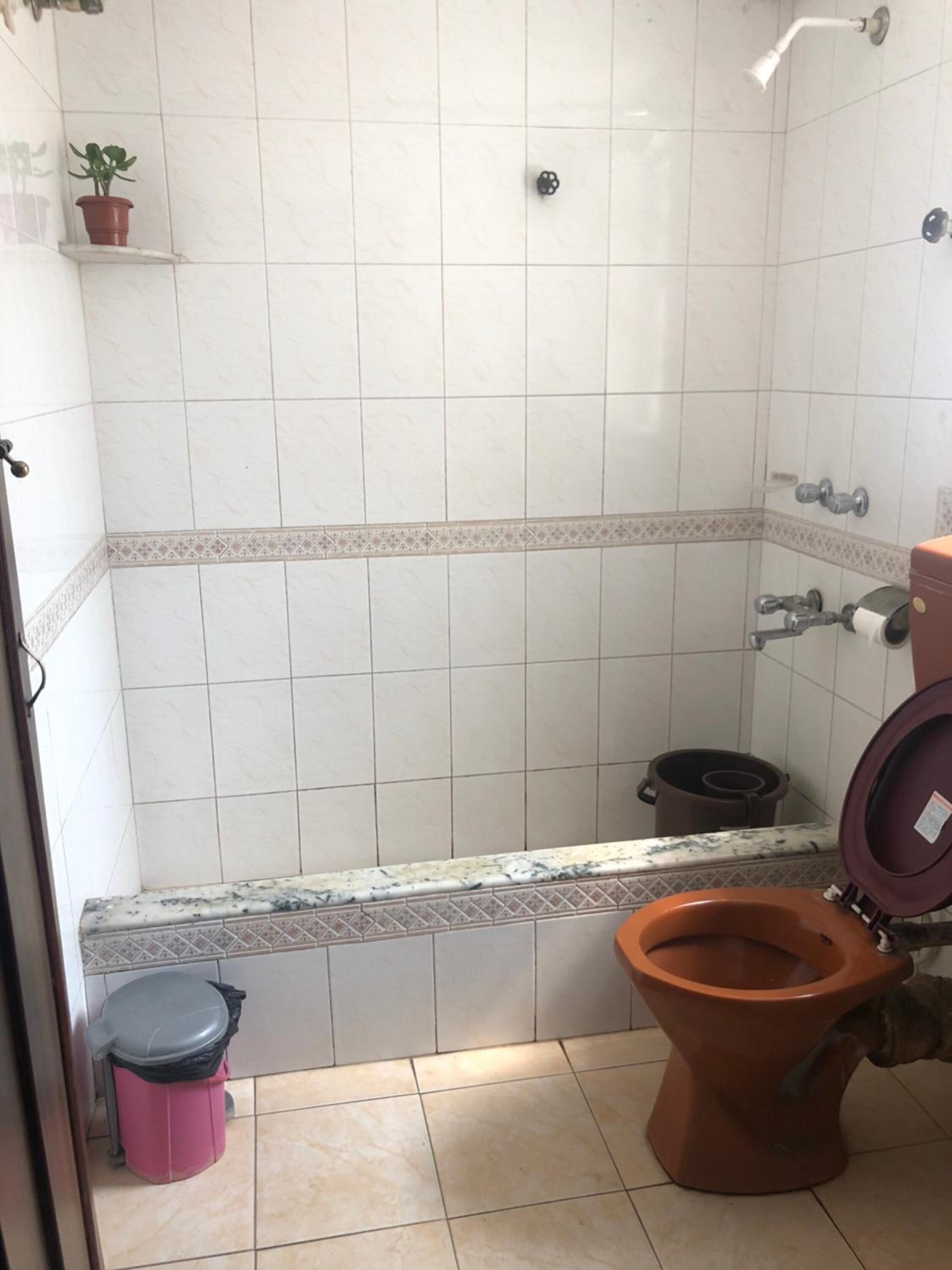 A bathroom with a shower, toilet, and trash bin.