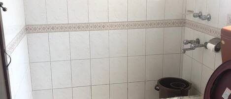 A bathroom with a shower, toilet, and trash bin.