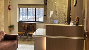 Una habitación de hotel moderna con pared de mármol, ventilador de techo, mostrador de recepción de madera y ventana con vista al exterior.