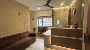 Un moderno vestíbulo de hotel con un sofá de cuero marrón, una recepción con mostrador de mármol, un ventilador de techo y un gran ventanal que proporciona luz natural.
