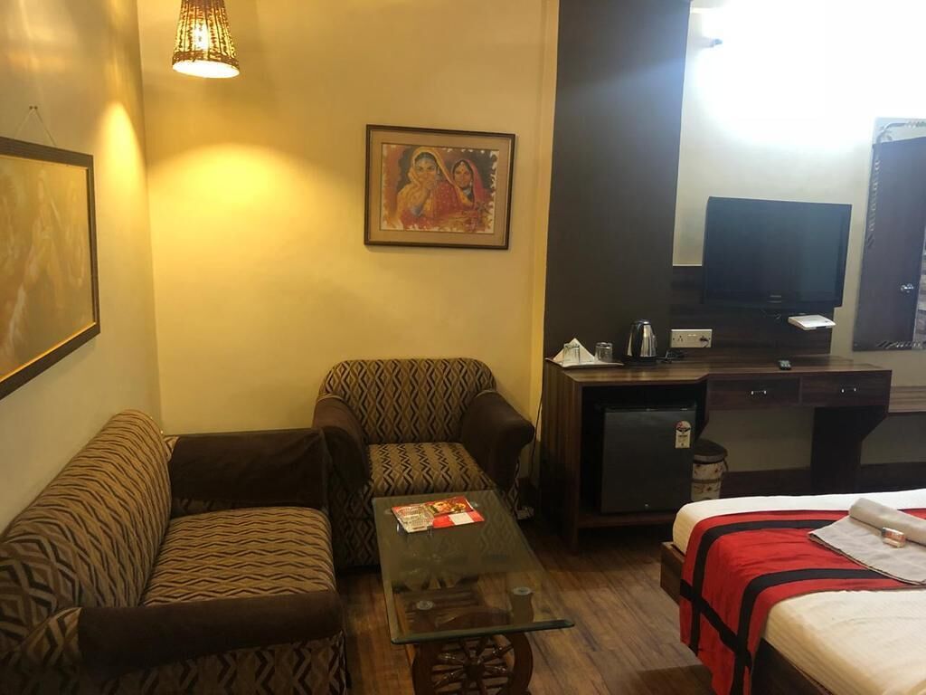 Une chambre d’hôtel avec des canapés à motifs, une table basse en verre, un lit recouvert d’une courtepointe rouge et noire, une télévision et un réfrigérateur.