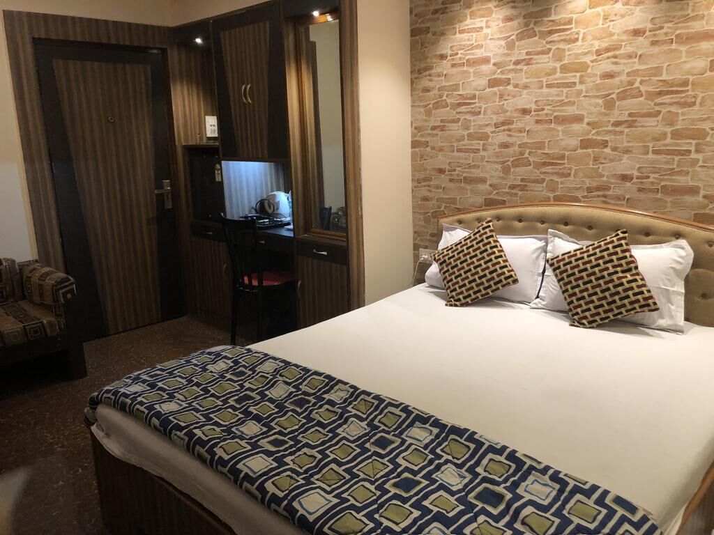 A hotel room with a bed, a desk with a computer, a chair, and a wardrobe.