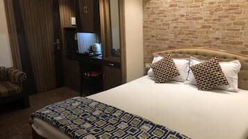 A hotel room with a bed, a desk with a computer, a chair, and a wardrobe.