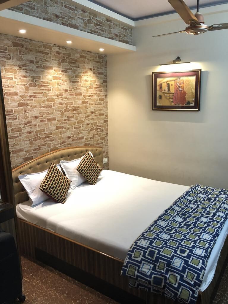 Un dormitorio con cabecera de ladrillo, cama con almohadas estampadas, ventilador de techo, iluminación empotrada y un cuadro enmarcado en la pared.