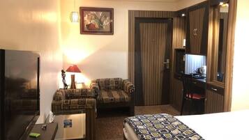 Habitación de hotel con cama, sofá, escritorio con lámpara, televisor y puerta con espejo.