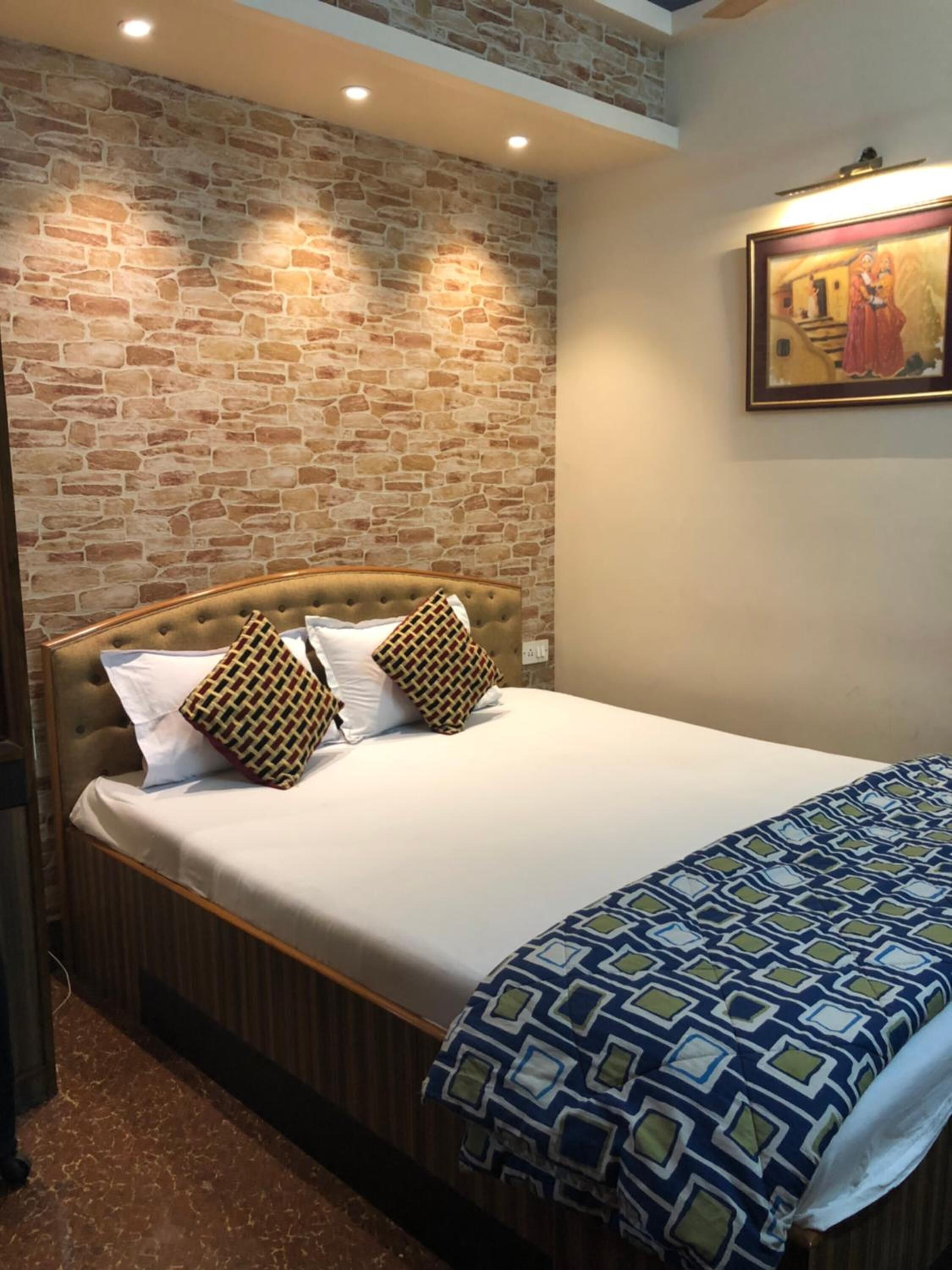 Un dormitorio con pared de ladrillo, cabecera acolchada y colcha estampada.