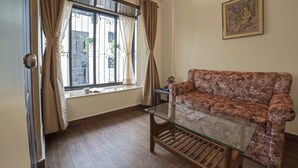 Una habitación con un sofá floral, una mesa de centro de vidrio, una ventana con cortinas y un cuadro en la pared.