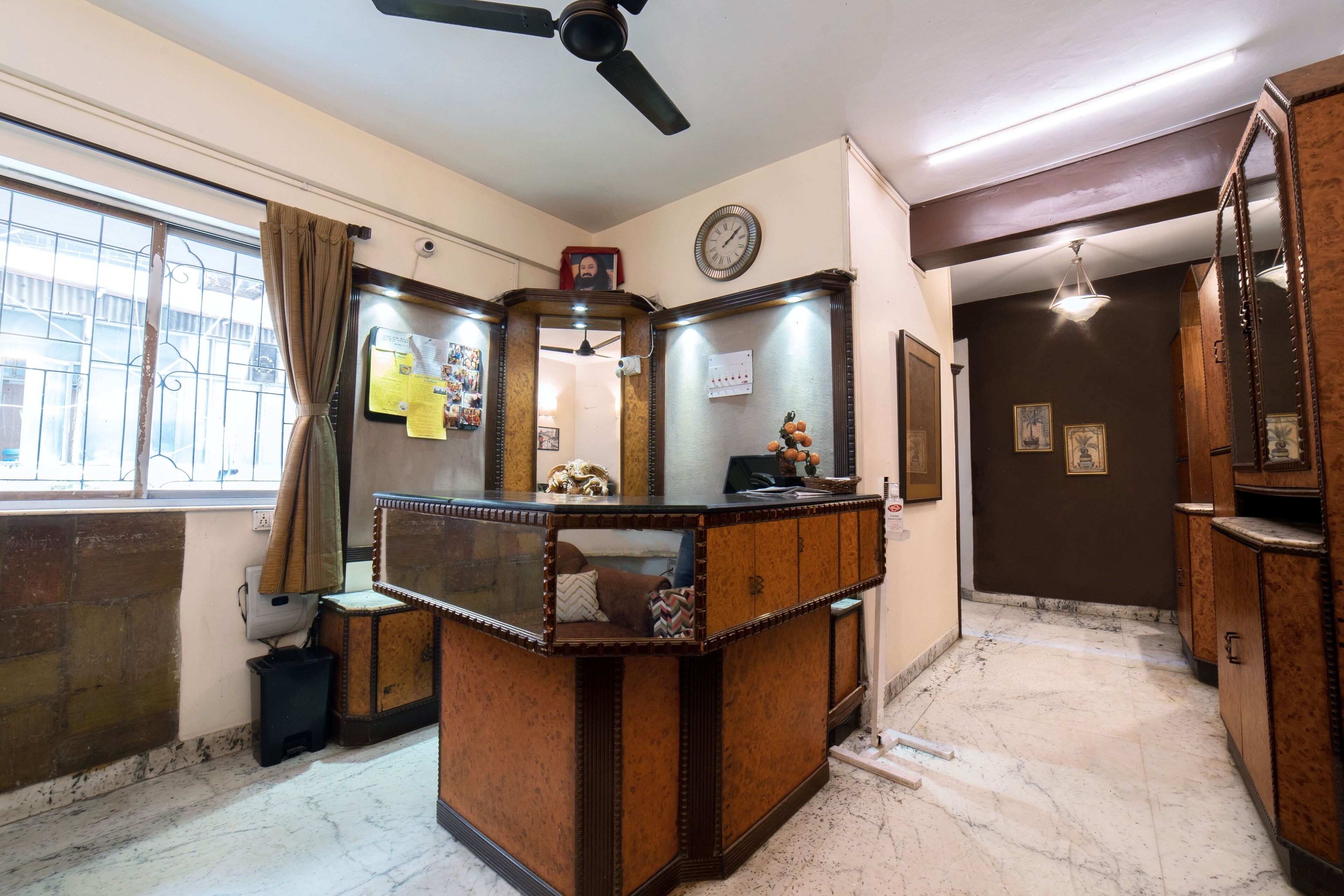 A room with a wooden desk, a ceiling fan, a clock, and a window with curtains.