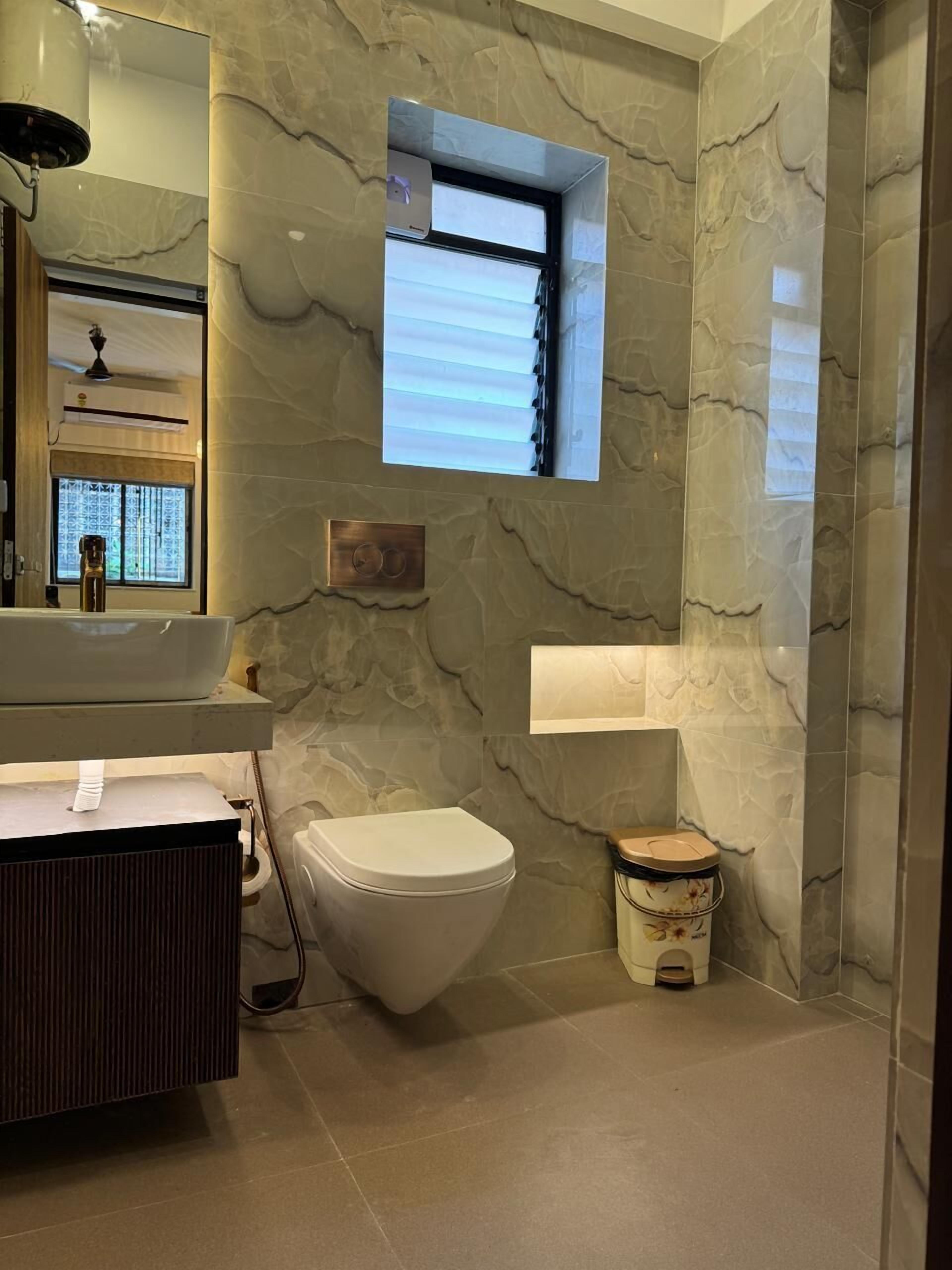 Un baño moderno con pared de mármol, lavamanos integrado, inodoro y un pequeño ventanal.