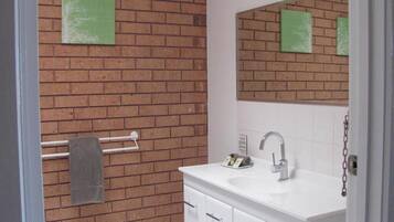 A bathroom with a brick wall, a white sink, a mirror, and a towel rack.