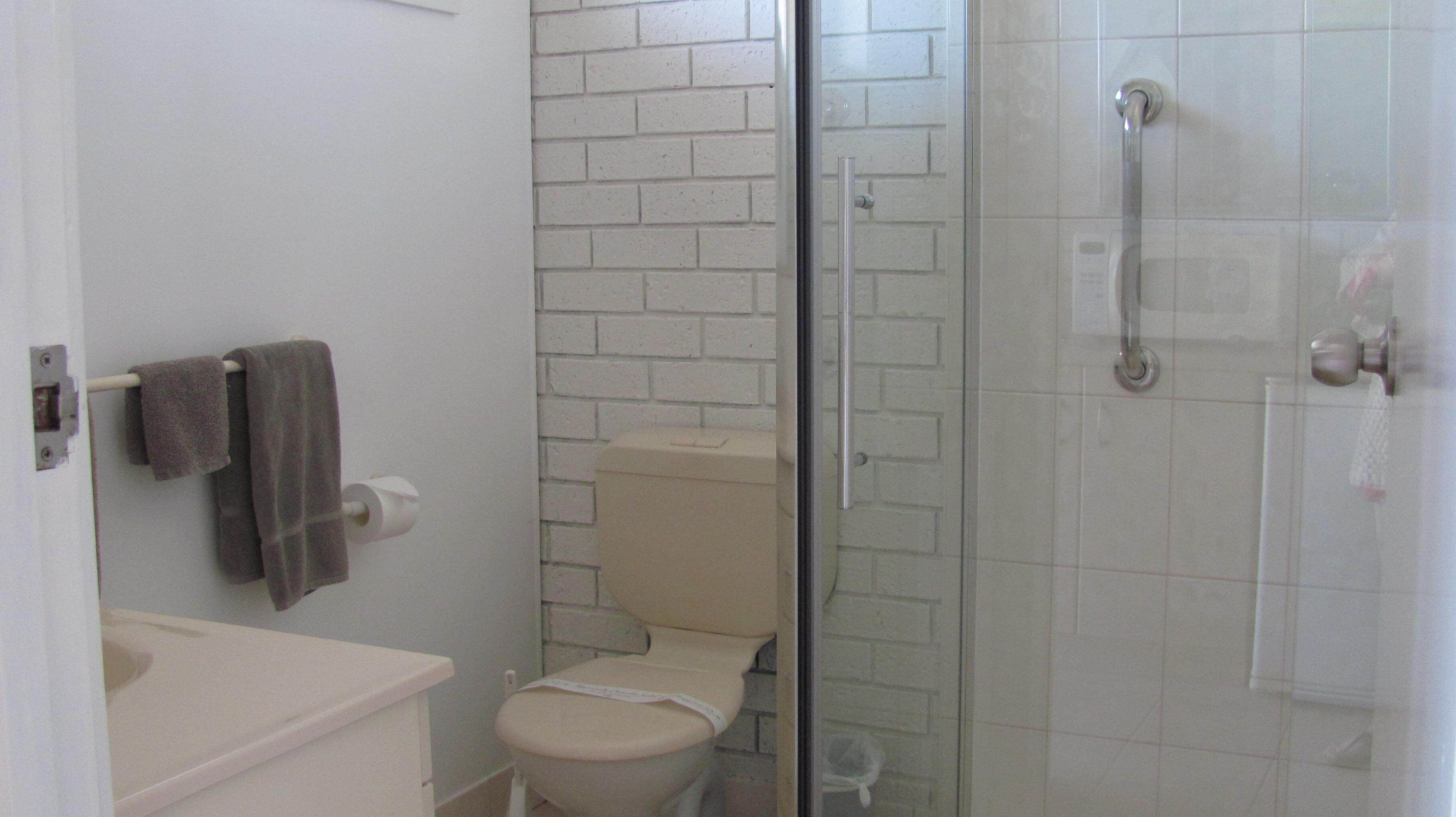 Une salle de bain équipée de toilettes, d’une douche à parois de verre et d’un porte-serviettes.