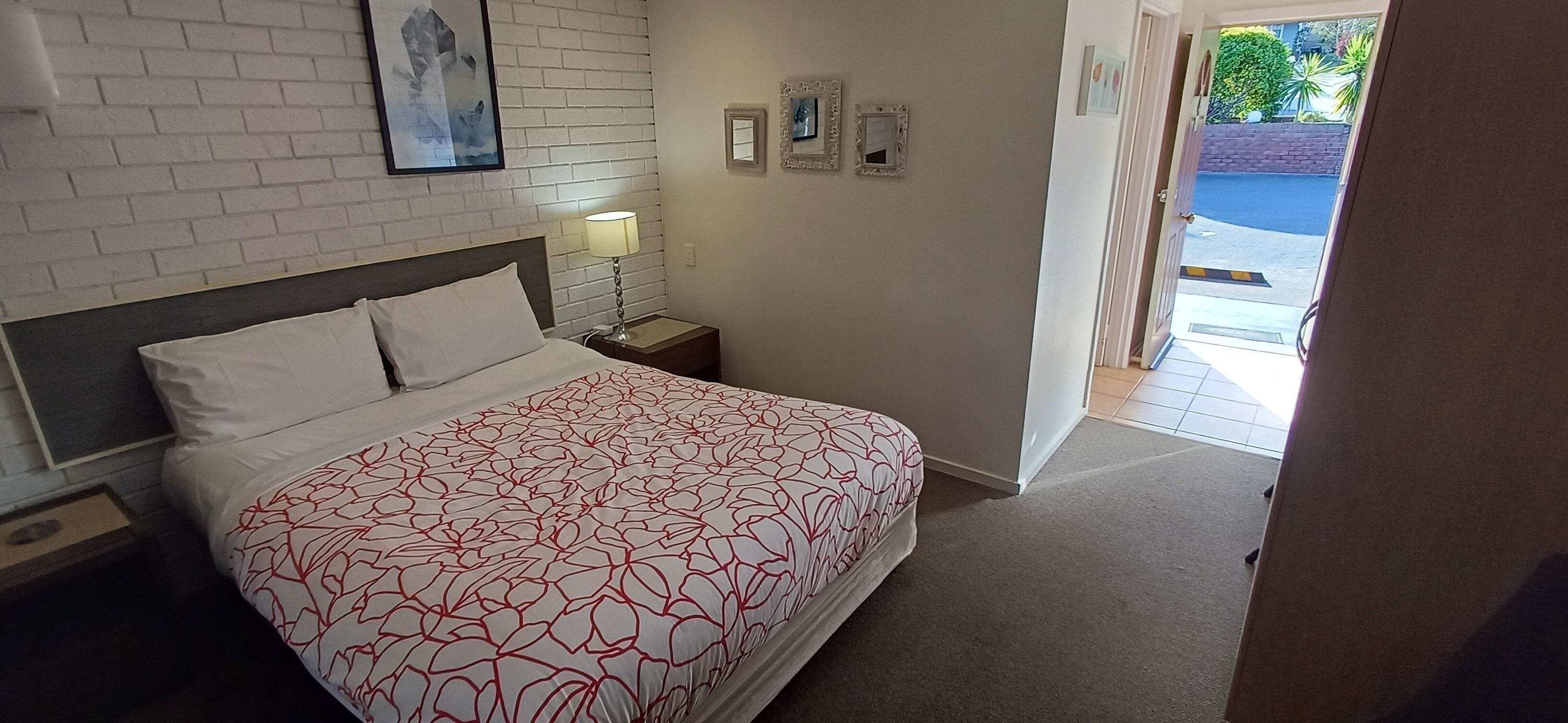 A hotel room with a bed, a nightstand, a lamp, and a door leading to a balcony.