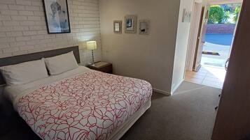 A hotel room with a bed, a nightstand, a lamp, and a door leading to a balcony.