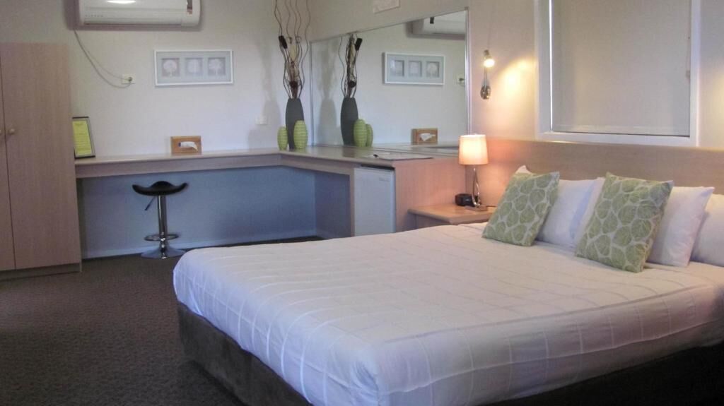 A hotel room with a bed, a desk, a chair, and a mirror.