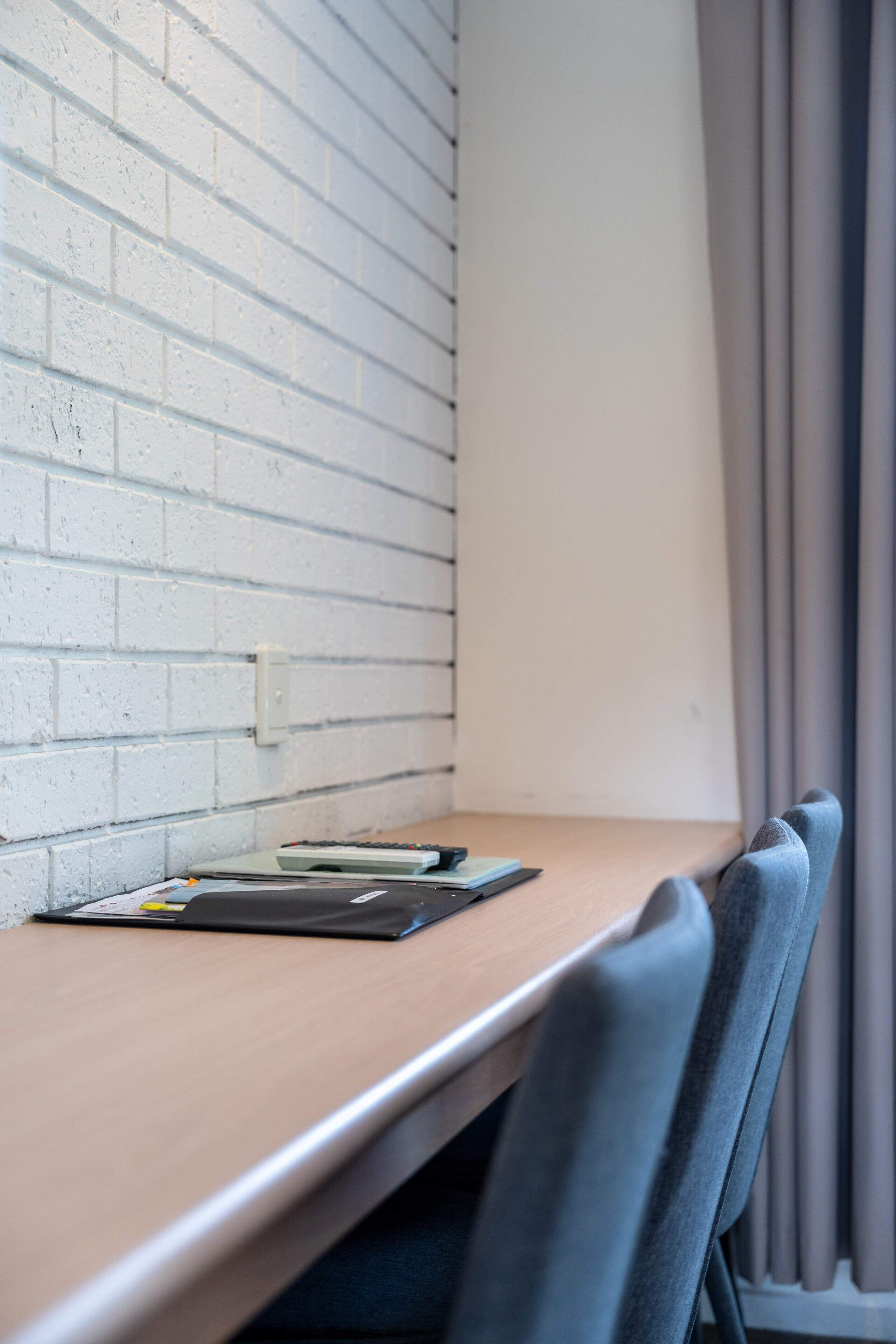 Une salle de conférence avec une table en bois, un mur en briques blanches et des rideaux gris.