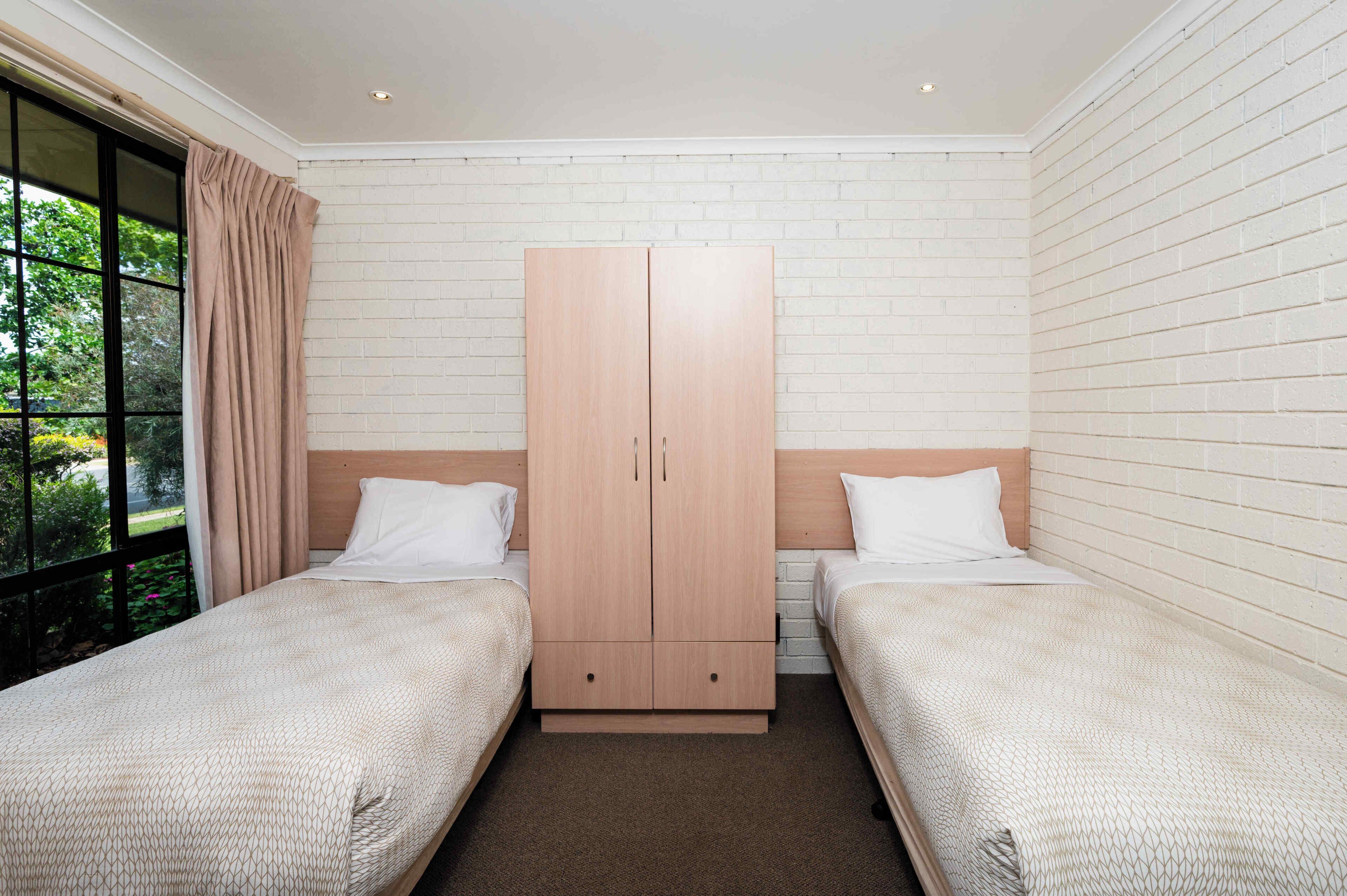 Un dormitorio con dos camas individuales, un armario de madera y una ventana con cortinas.