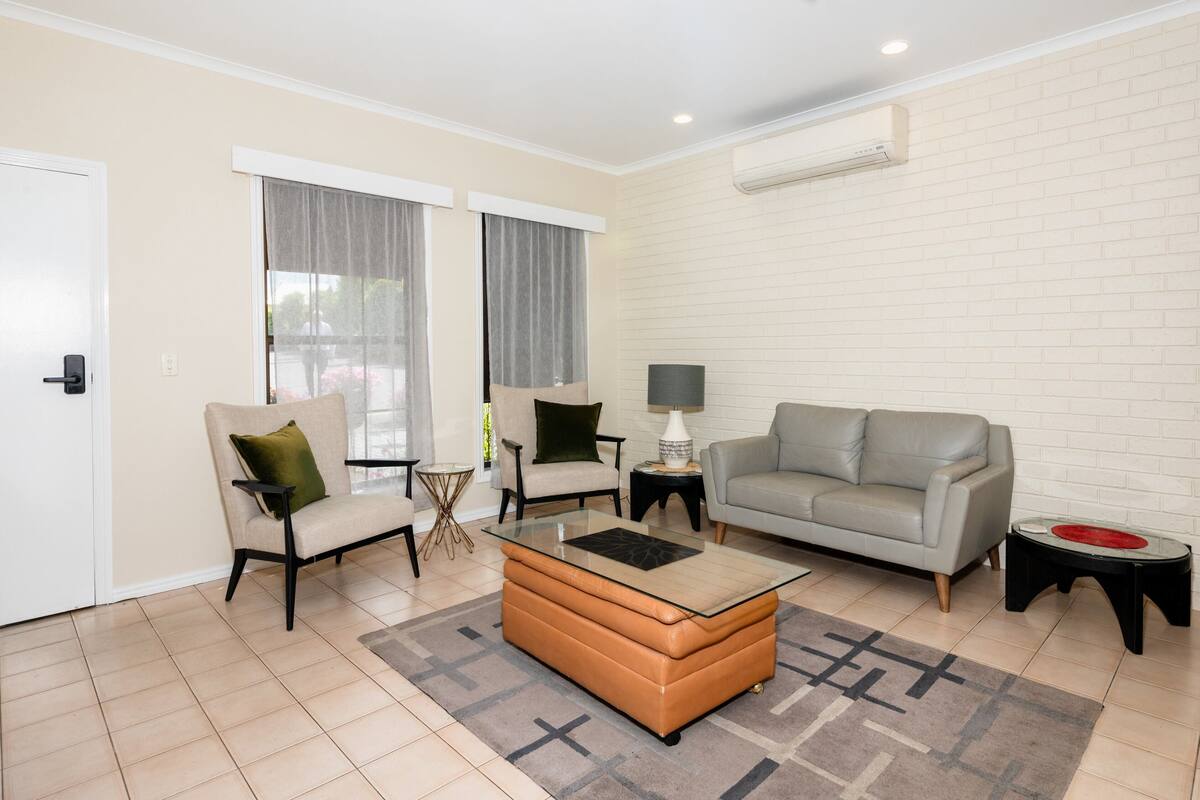 A modern living room with a sofa, armchairs, a glass coffee table, and a small side table.