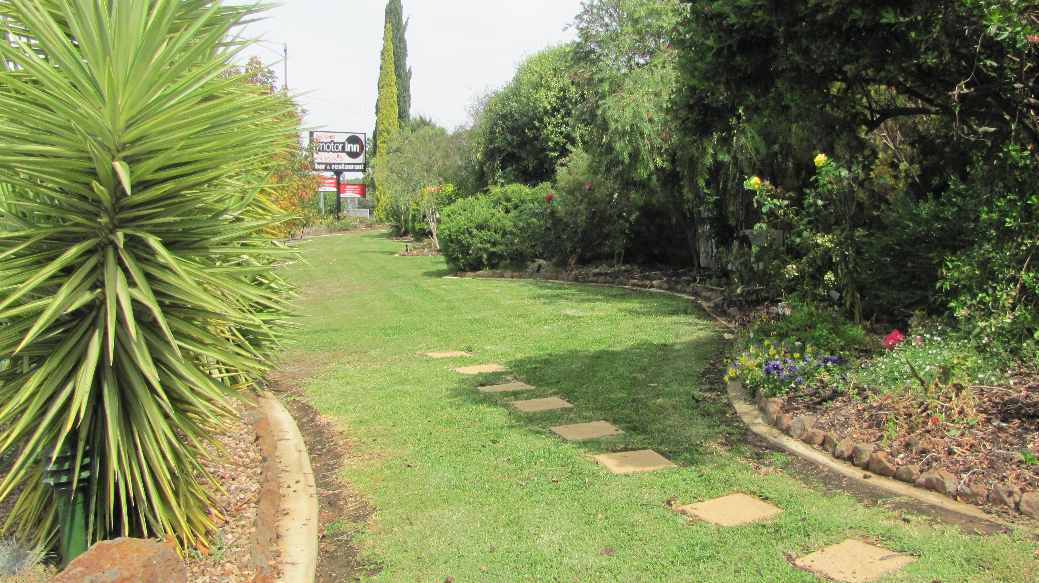 A well-maintained garden path with stepping stones, surrounded by lush greenery and a sign for a motor inn.