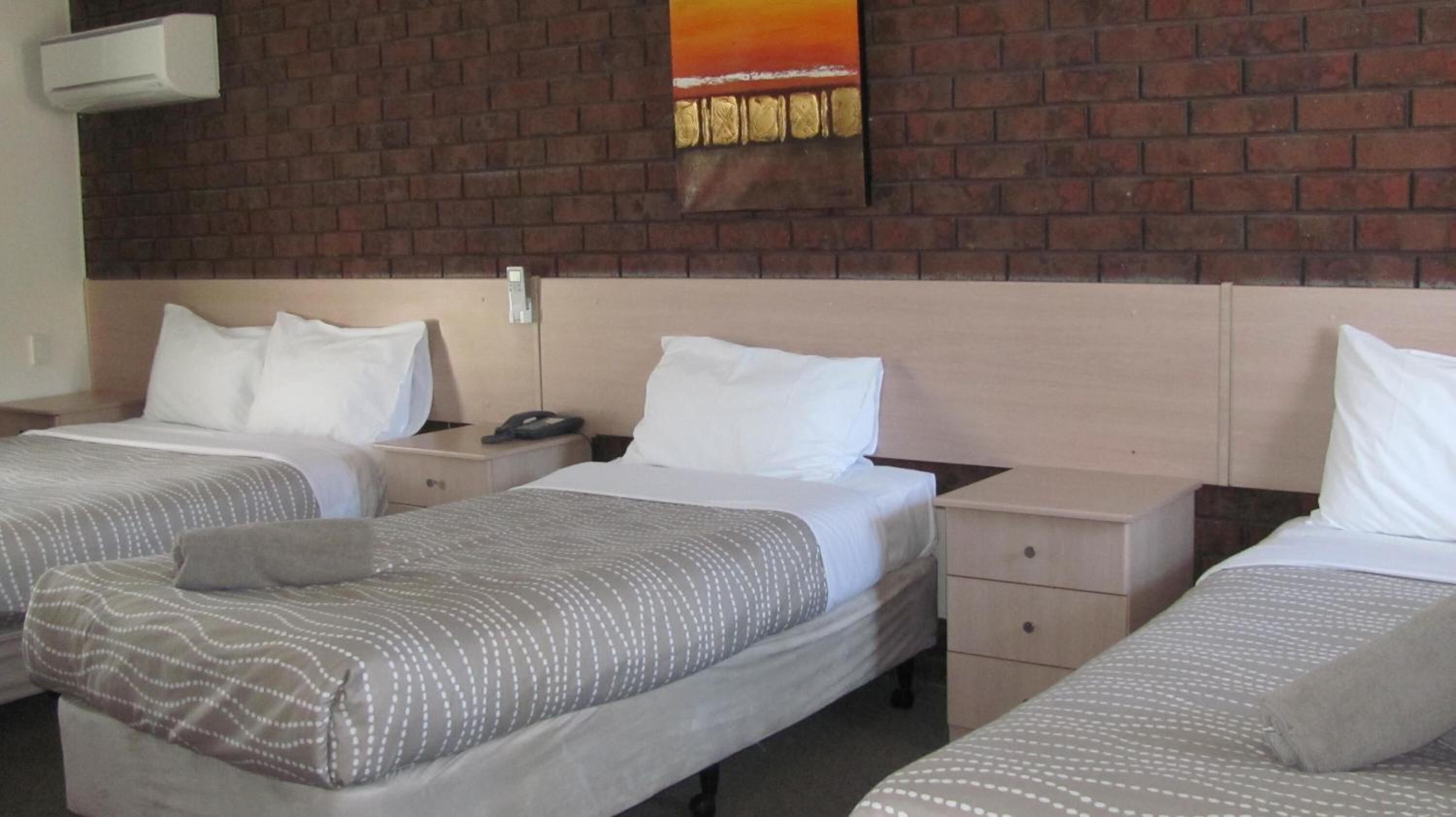 Una habitación de hotel con dos camas individuales, una pared de ladrillo, un cuadro y un teléfono en la mesita de noche.