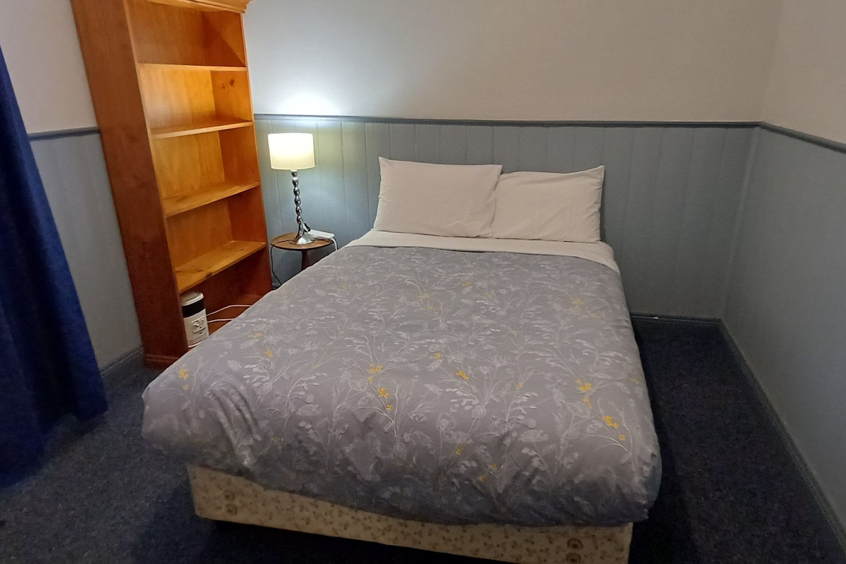 A bedroom with a bed, a bedside lamp, a wooden shelf, and a blue curtain.