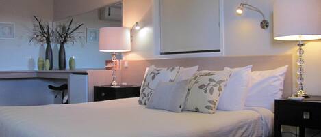 Una habitación de hotel con una cama, una mesita de noche, una lámpara, un espejo y un florero con flores sobre la cómoda.