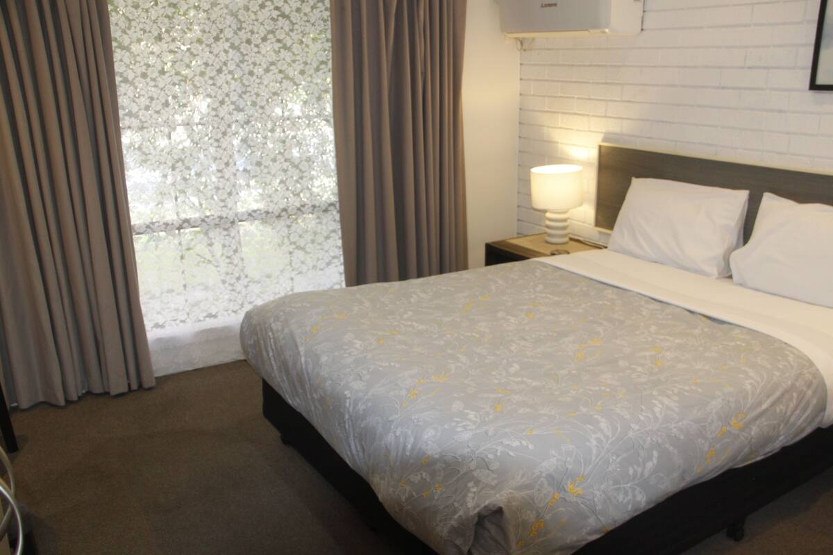 A hotel room with a bed, curtains, a nightstand, a lamp, and a window with a view.