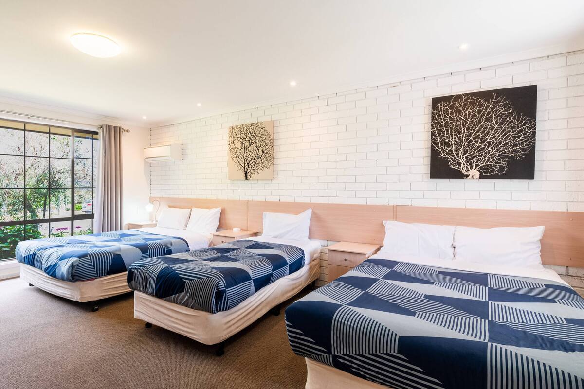 A hotel room with three beds, white brick walls, and two wall art pieces.