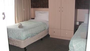 Een enkel bed met een opgerolde handdoek, een houten garderobe en een bakstenen muur op de achtergrond.
