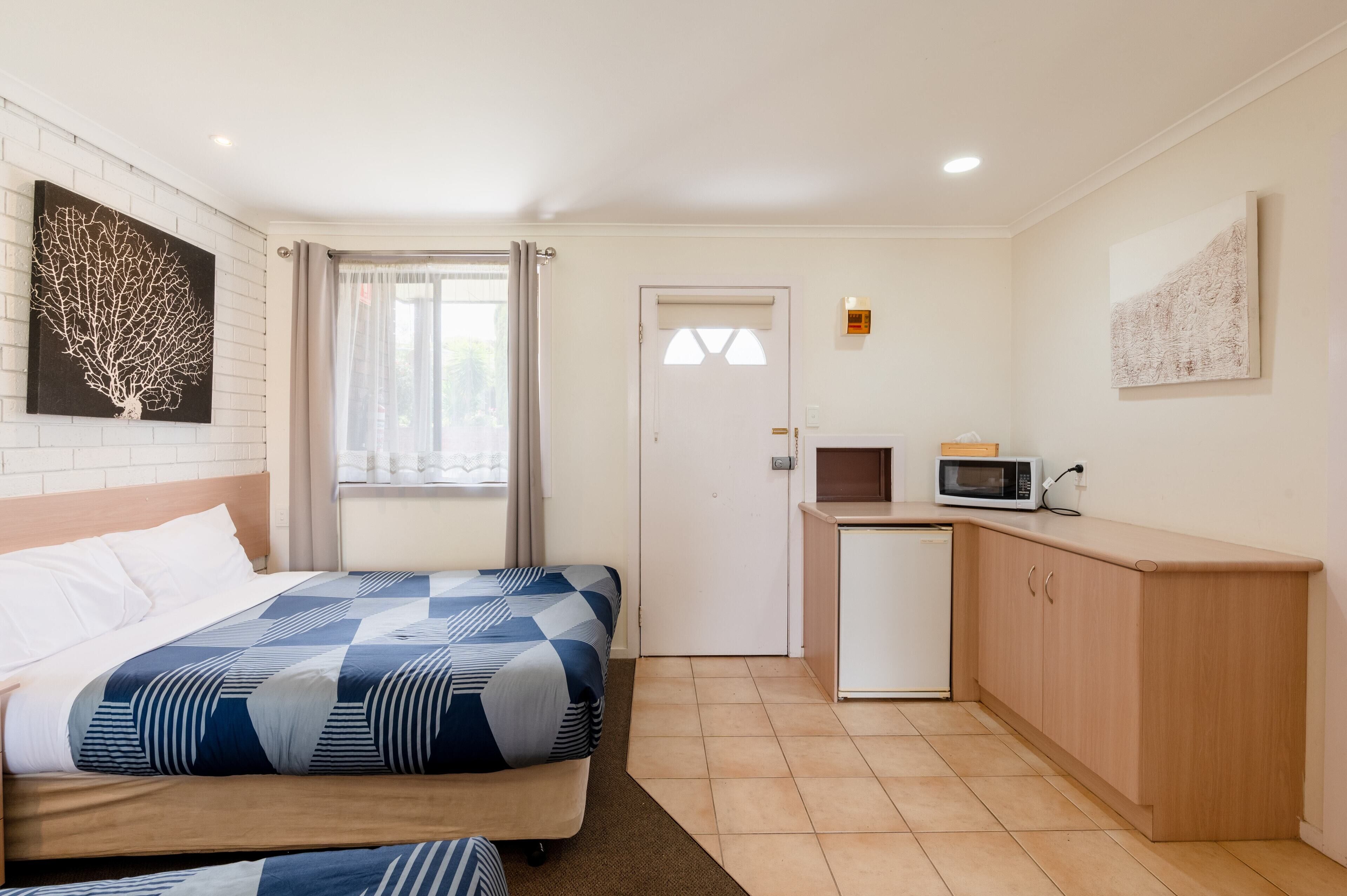 Habitación de hotel con cama, una kitchenette pequeña, una puerta y una ventana con cortinas.