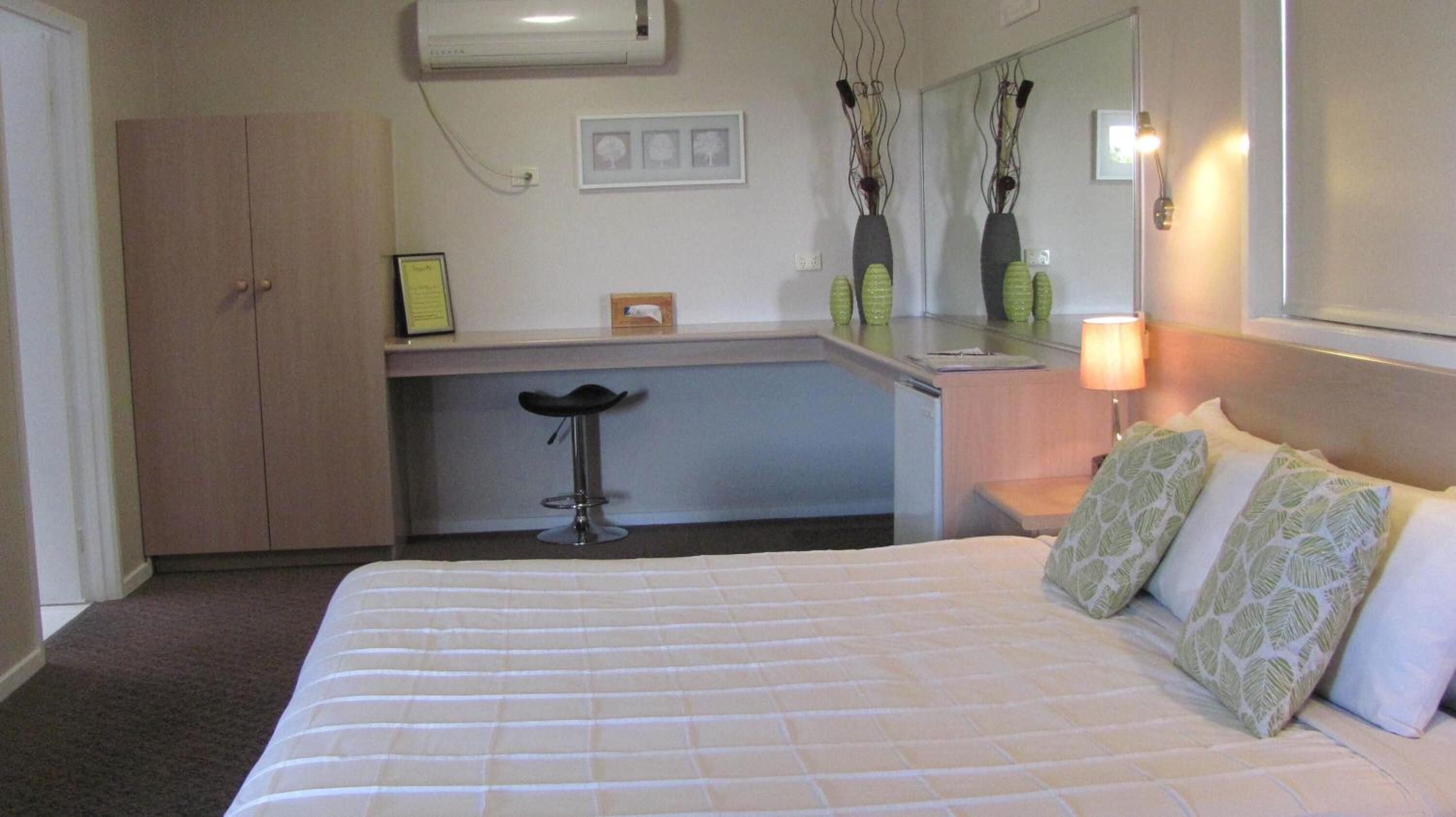 Una habitación de hotel con una cama, un escritorio, una silla, un espejo y un armario.
