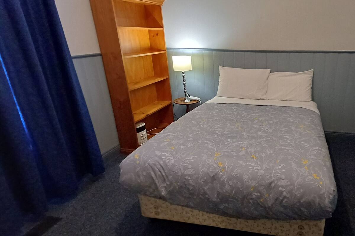A bedroom with a bed, a bedside lamp, a wooden shelf, and a blue curtain.
