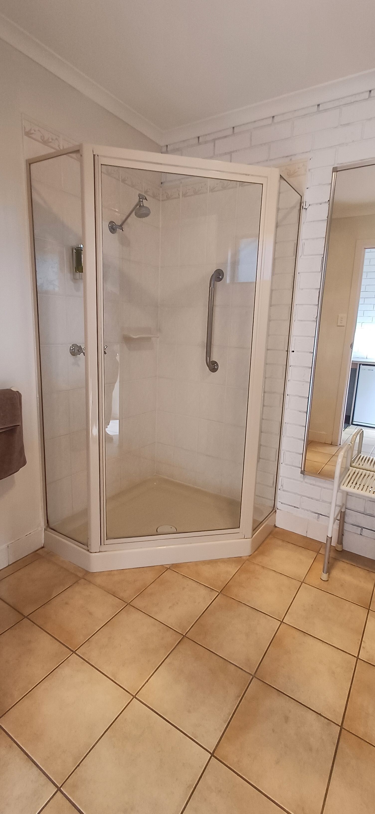 Un espace de douche d’angle avec une porte en verre, une barre d’appui et un sol carrelé.