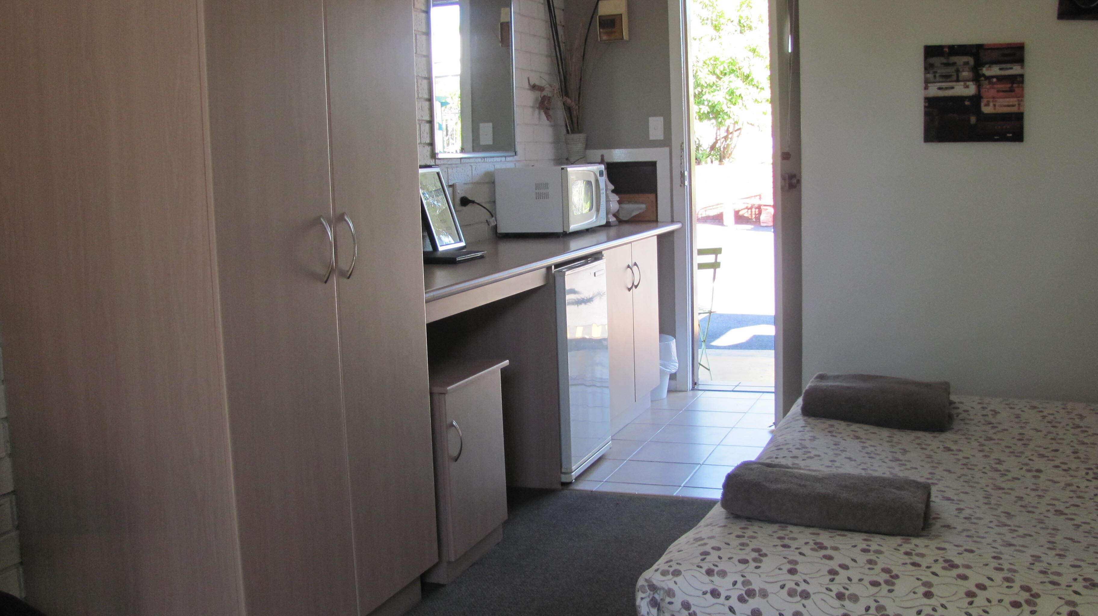 A compact kitchen with a microwave, refrigerator, and a small sink. There is a bed with a floral bedspread and two pillows.