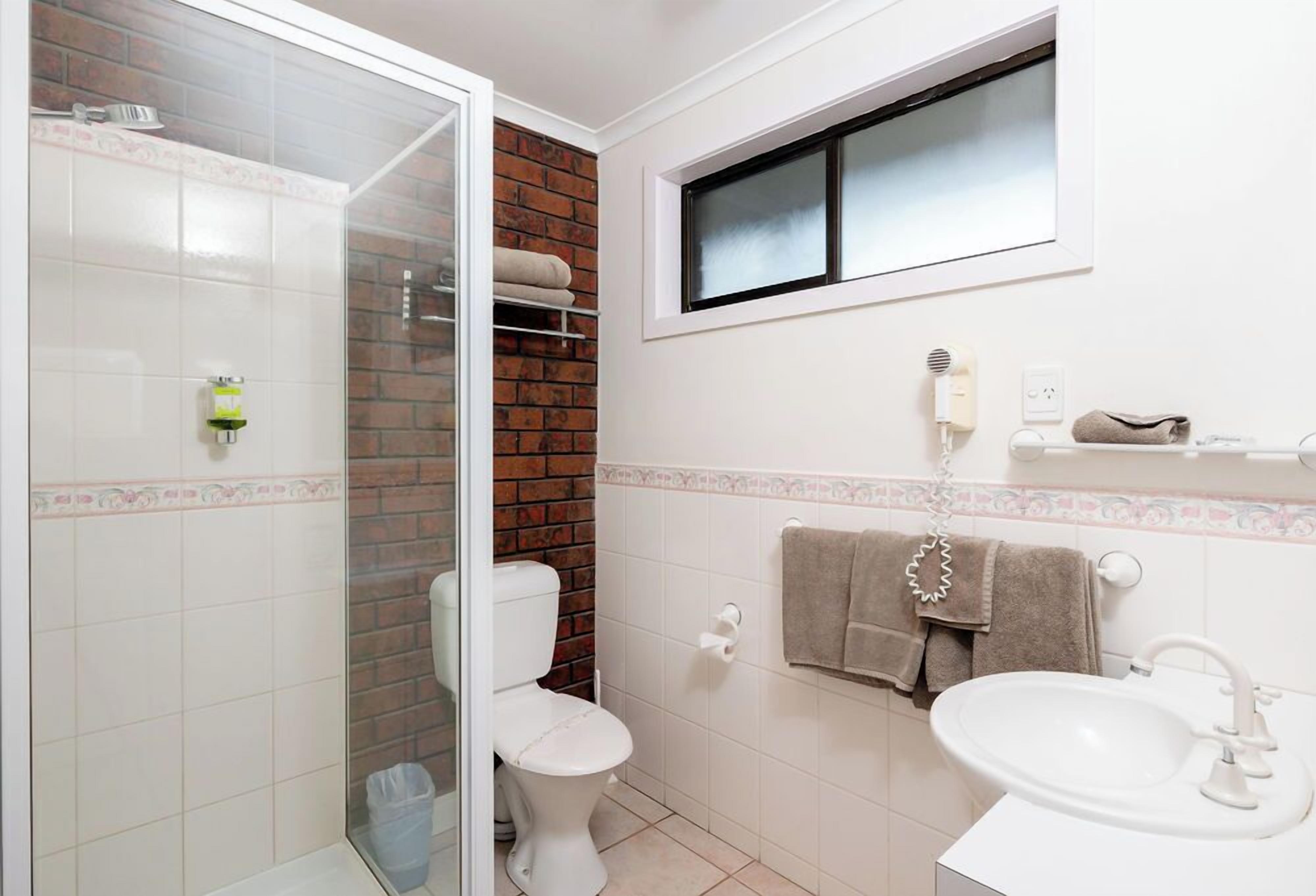 A bathroom with a shower, toilet, sink, and a window.