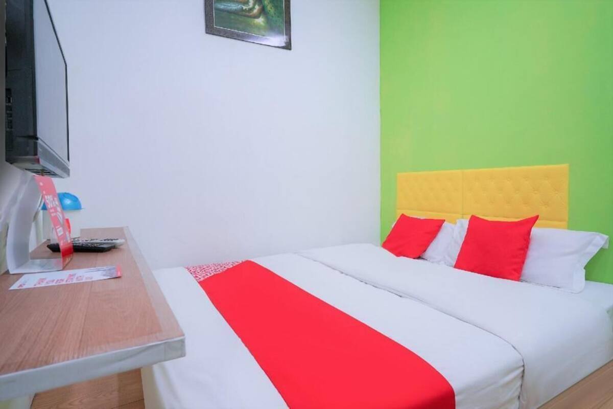 Une chambre d’hôtel avec un lit, une télévision, un bureau et un mur vert.