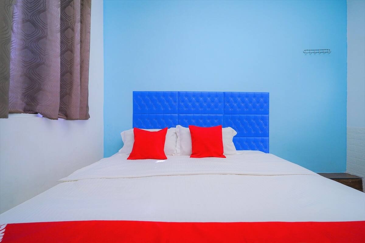 Un lit avec une tête de lit bleue, une literie blanche et deux oreillers rouges.