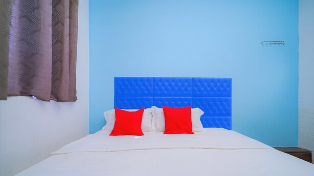 A bed with a blue headboard, white bedding, and two red pillows. - Hotel O V Stay Guesthouse (George Town)