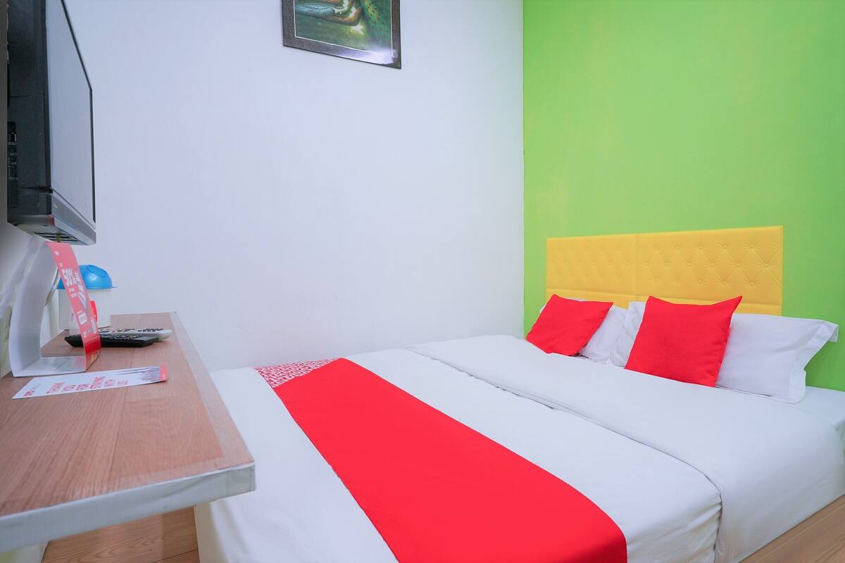 Une chambre d’hôtel avec un lit, une télévision, un bureau et un mur vert.
